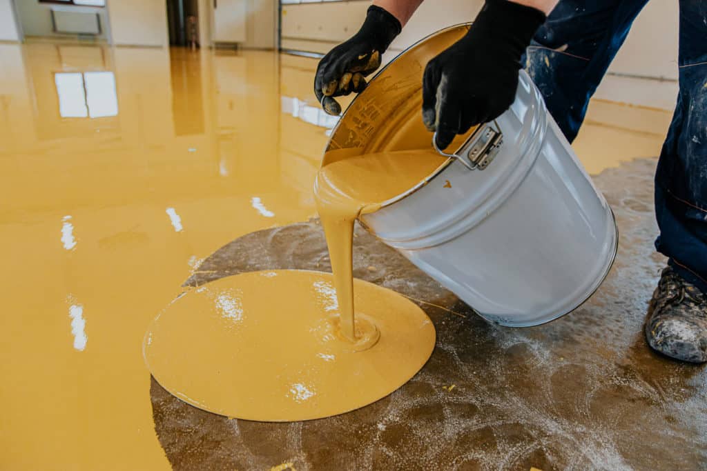 Worker spilling yellow paint from bucket on floor.