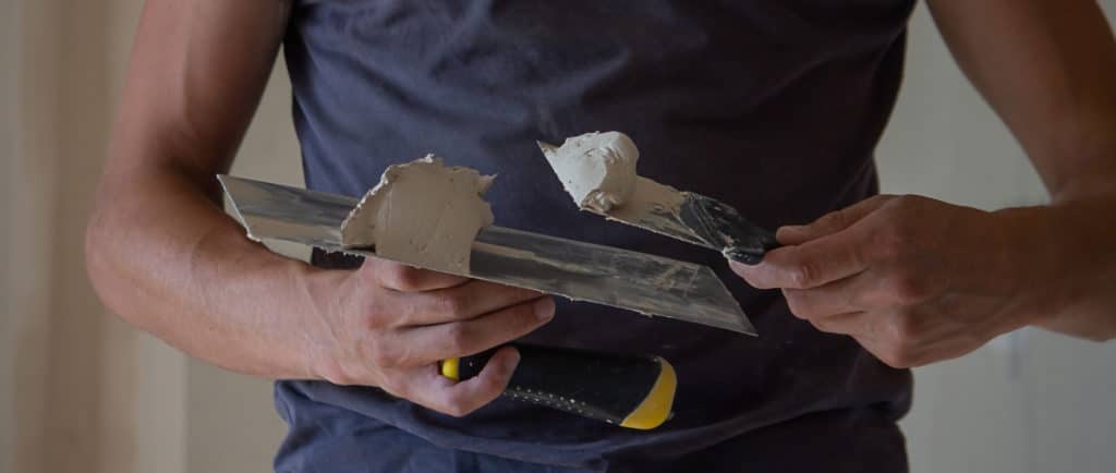 Person holding drywall putty knives with spackle.