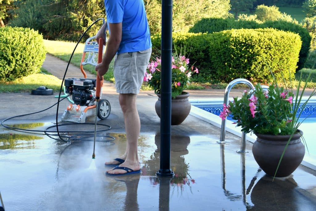 Man pressure washing patio near pool.