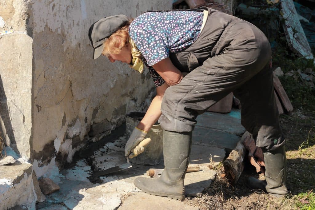 Woman repairing wall outdoors.