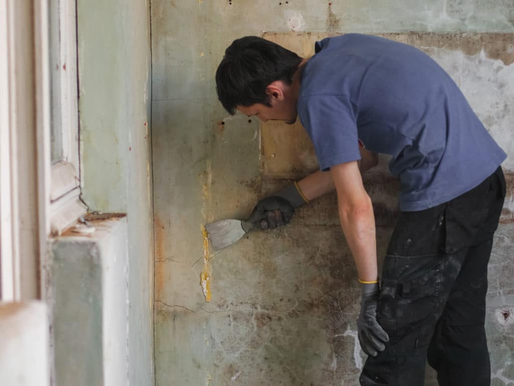 Man scraping old paint off wall during renovation.