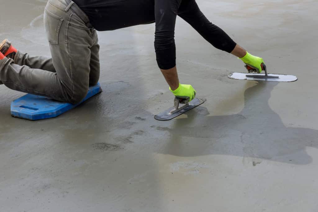 Worker smoothing concrete with trowels.