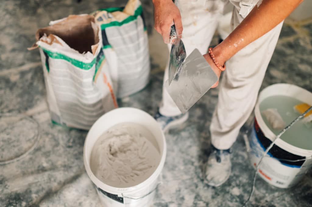 Painter mixing compound in buckets on construction site.