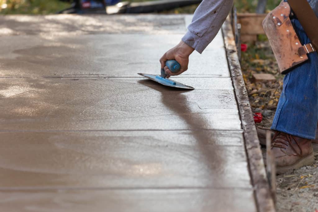 Worker smoothing wet concrete on sidewalk.