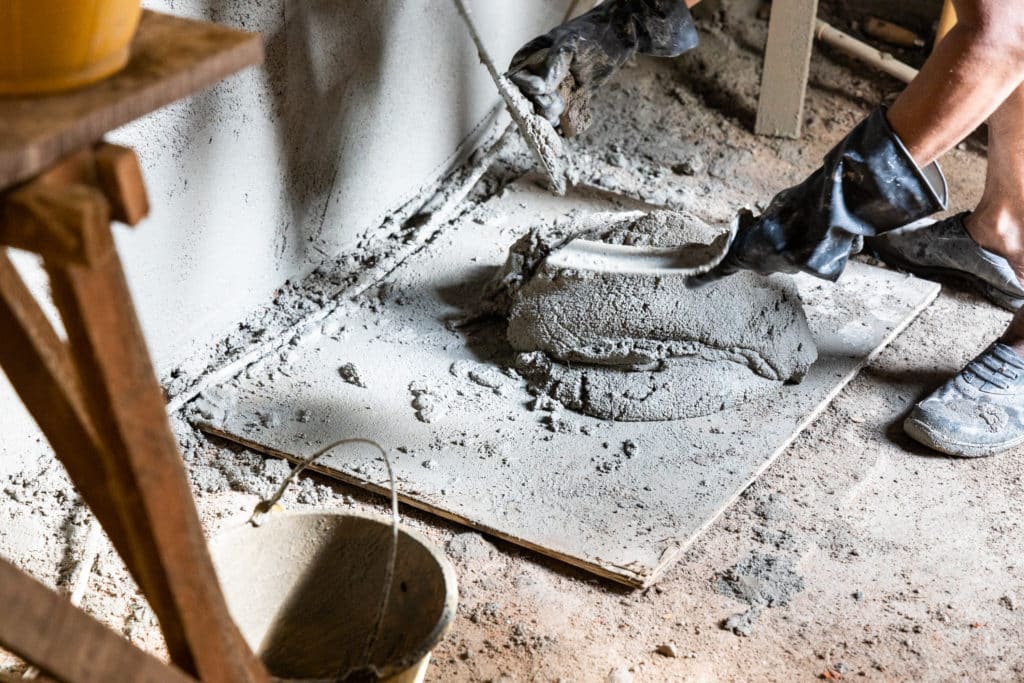 Worker spreading concrete on construction site floor.