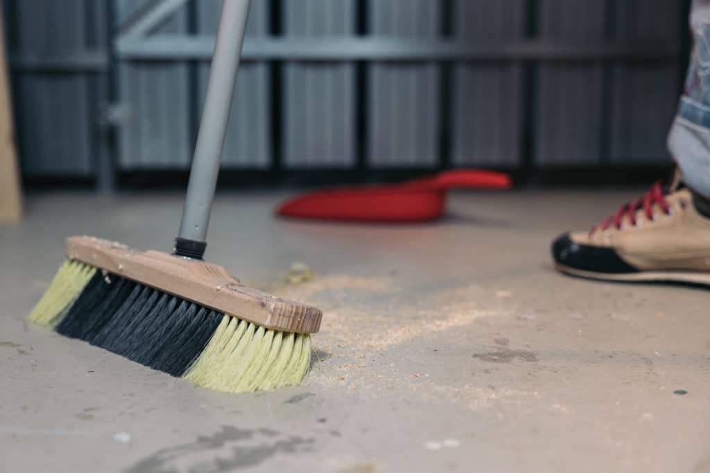 Person sweeping floor with broom near dustpan.