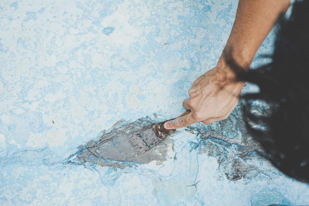 Person repairing a crack in blue surface.