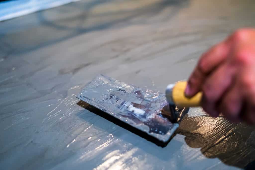 Applying epoxy with a trowel on floor.