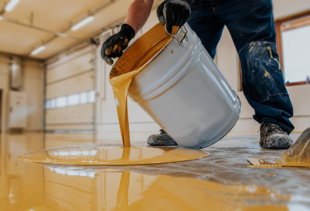 Person spilling yellow paint from bucket on floor.