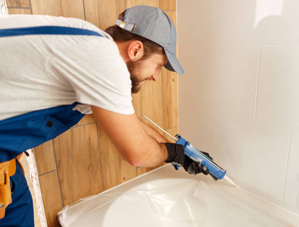 Worker applying caulk to bathtub tiles.