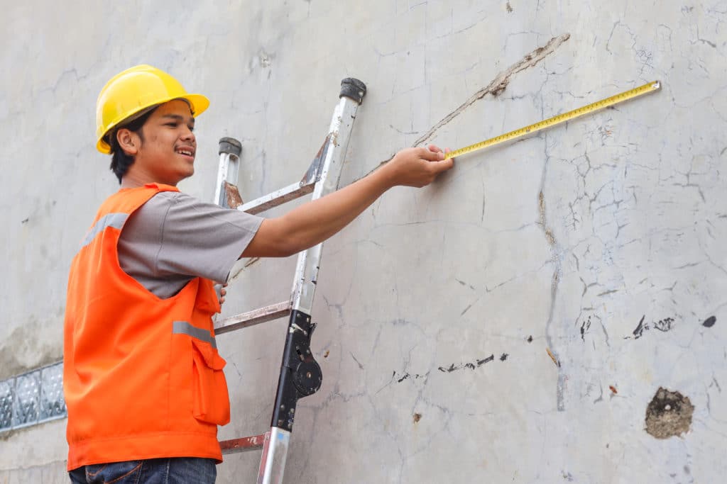 Worker measuring crack on wall with tape measure.