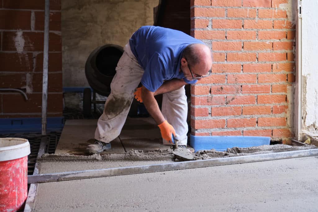 Worker smoothing concrete floor near brick wall.