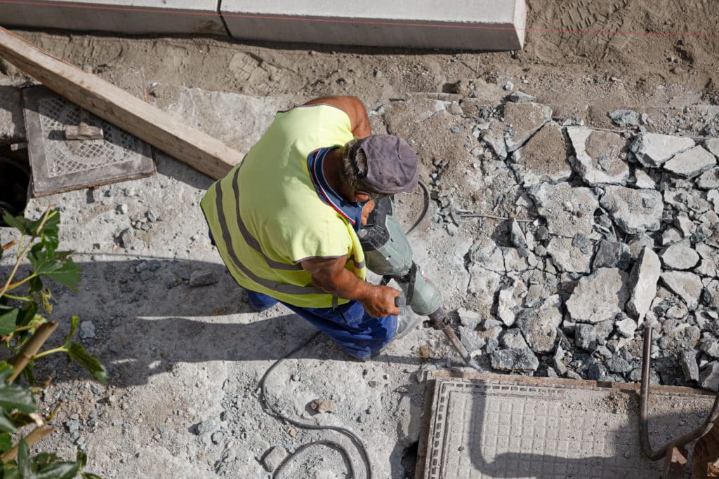 Worker using jackhammer on concrete surface.