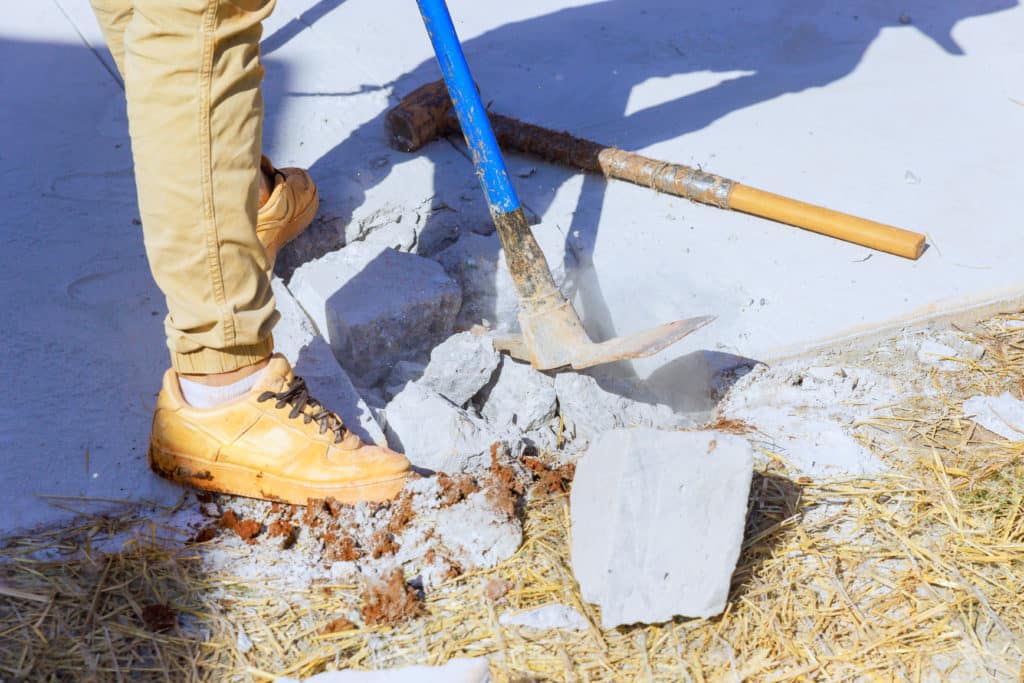 Person breaking concrete with pickaxe and shovel.
