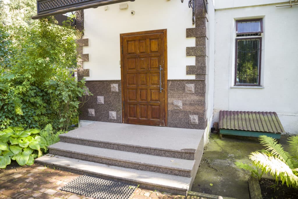 Wooden door entrance with stone steps and greenery.