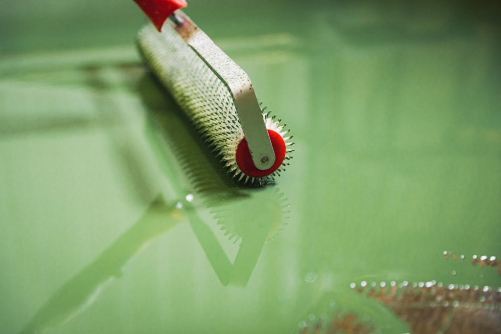 Paint roller applying green paint on wall.