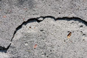 Cracked gray concrete surface with pebbles and leaf.