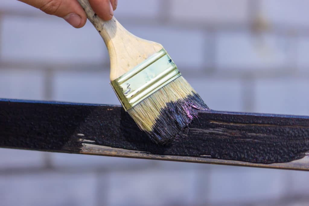 Paintbrush applying black paint to wooden surface.