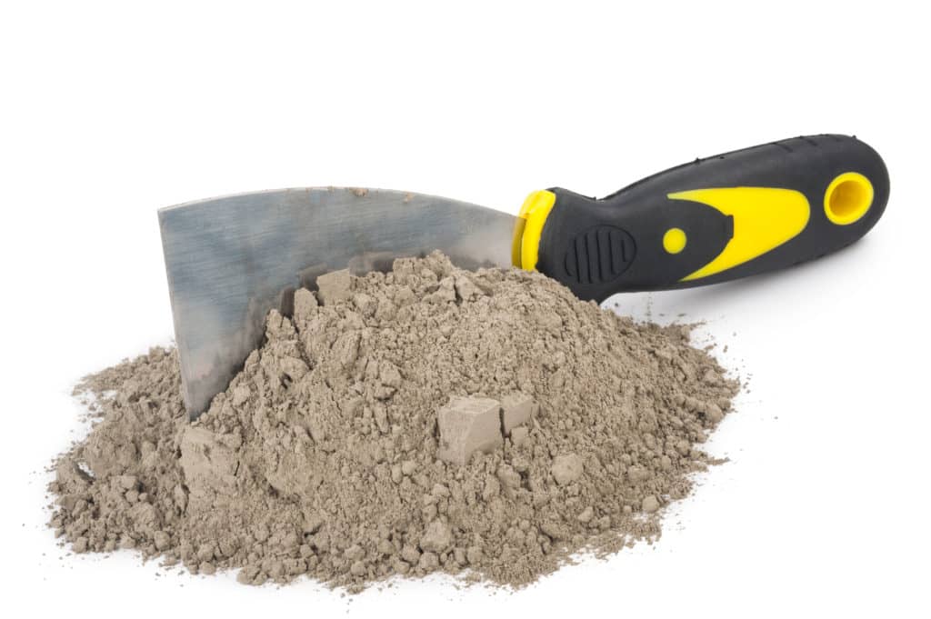 Putty knife with yellow-black handle on construction sand.