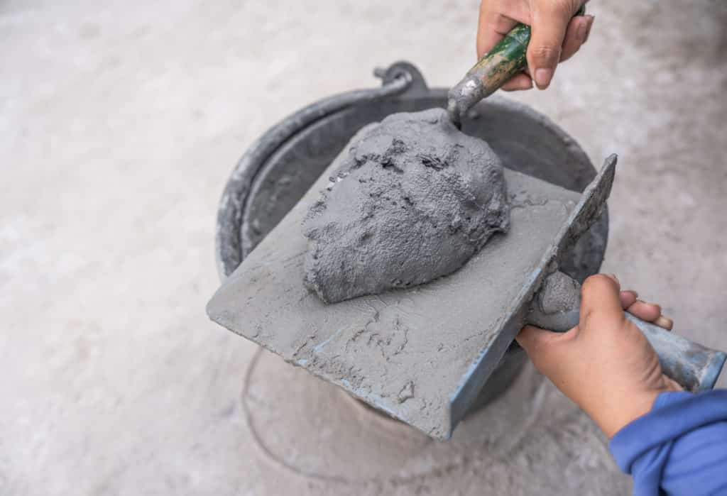 Worker scooping wet concrete with trowel.