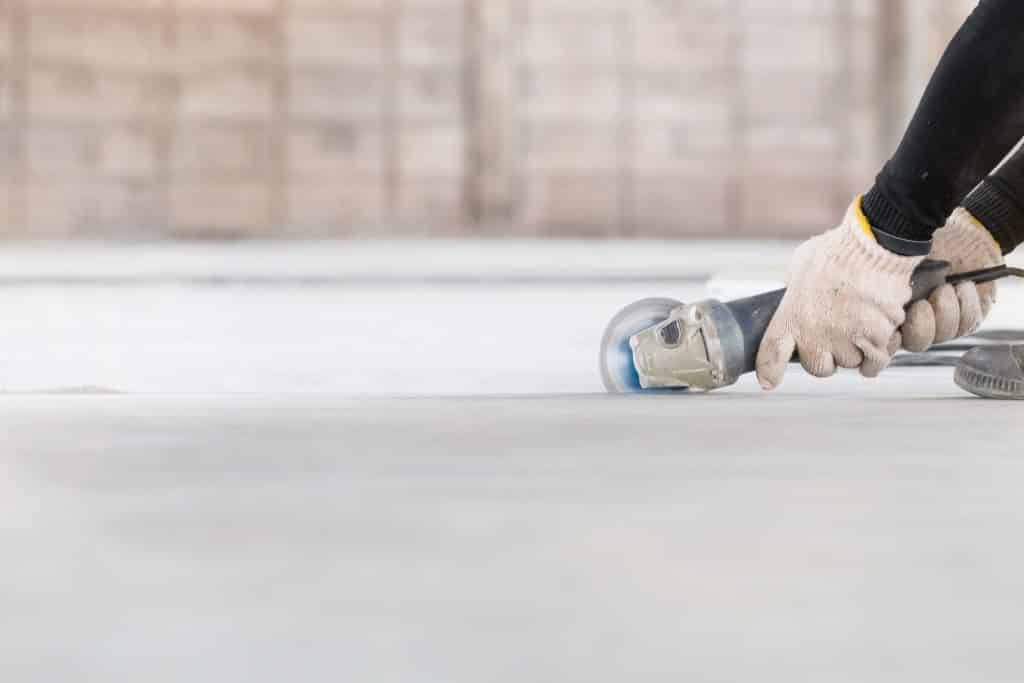 Worker using angle grinder on floor.