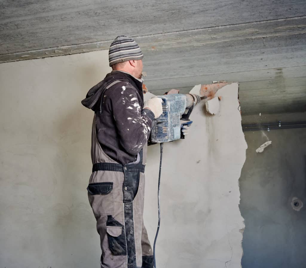 Worker using jackhammer on wall during renovation.