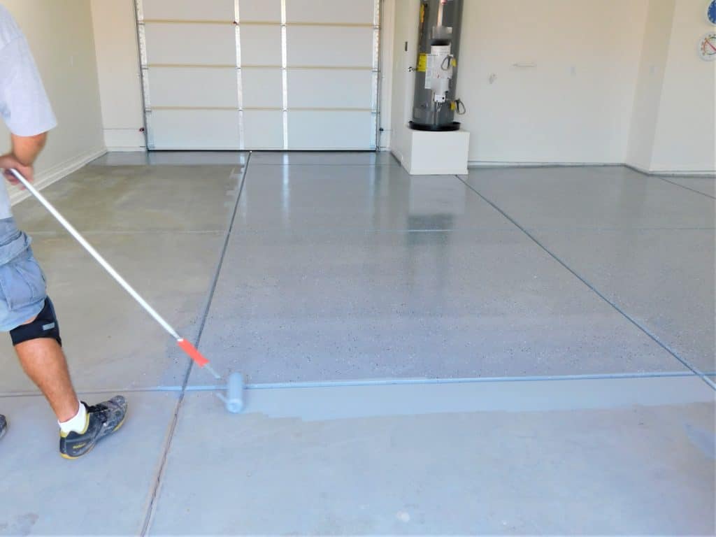 Person applying epoxy coating to garage floor.