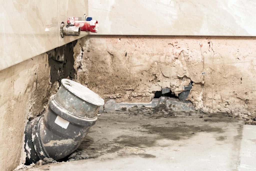 Damaged wall and piping with overturned bucket.