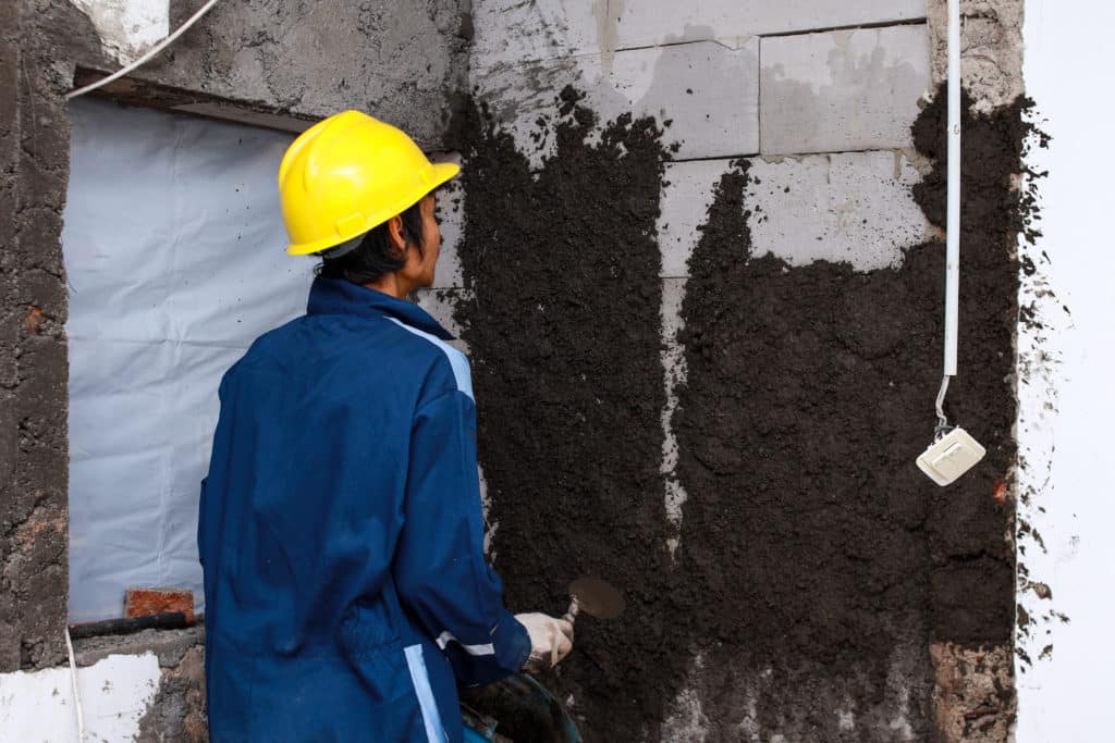 Worker applying cement to wall in construction site.