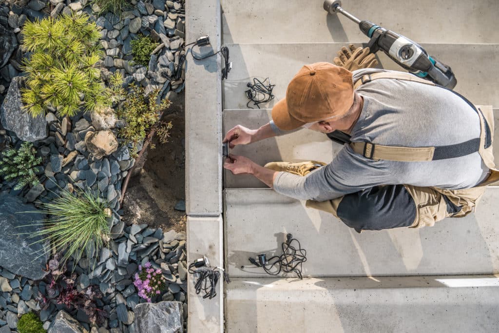 Worker installing outdoor lighting near landscaping rocks.