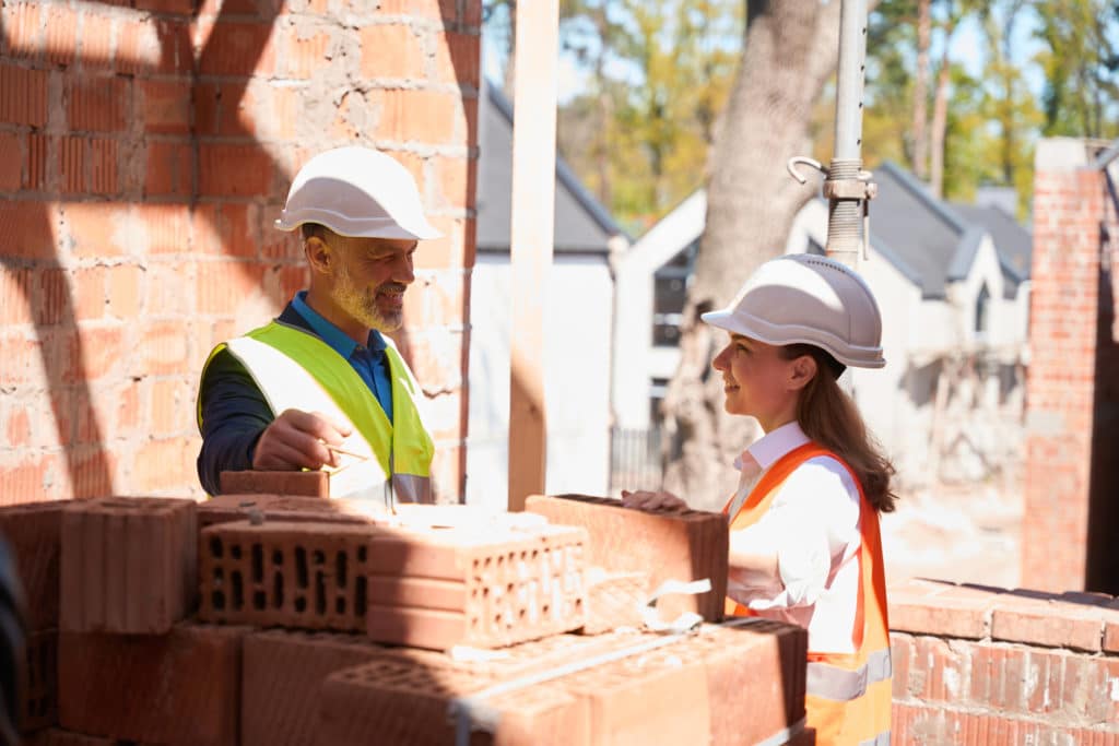 Construction workers discussing near brick wall on site.