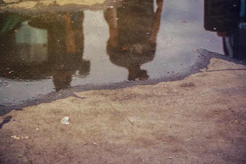 Reflection of two people in puddle on street.