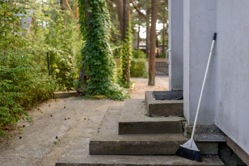 Broom leaning against a house near concrete steps.