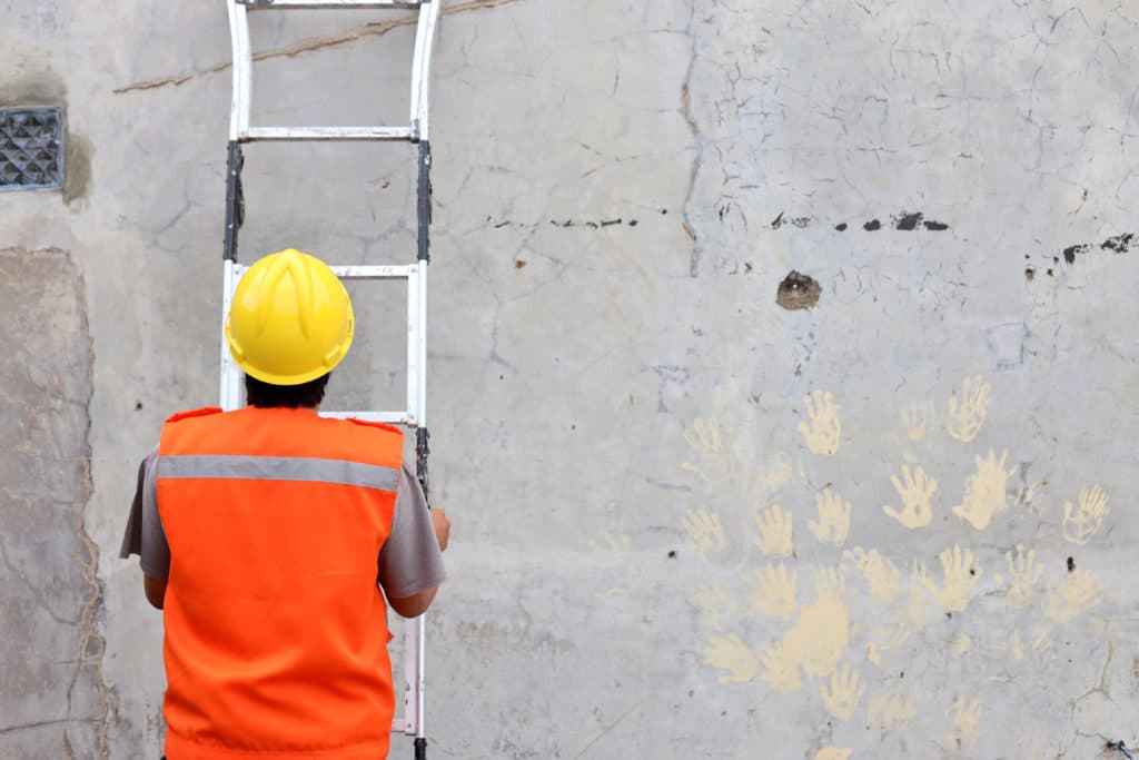 Worker in hard hat with ladder and handprints on wall.