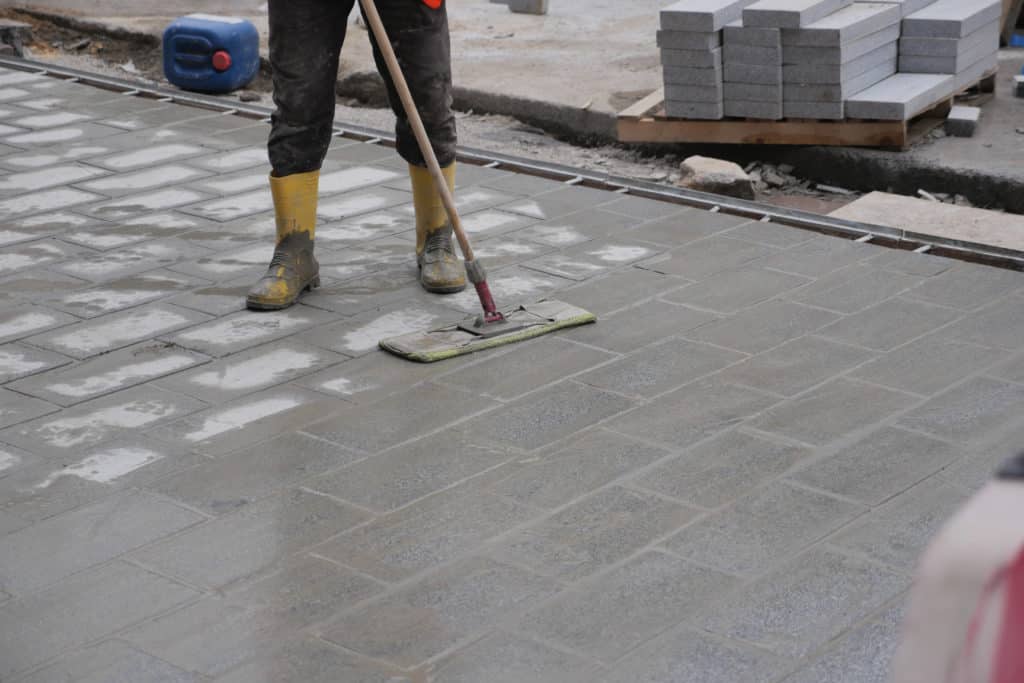 Worker smoothing pavement with squeegee on construction site.