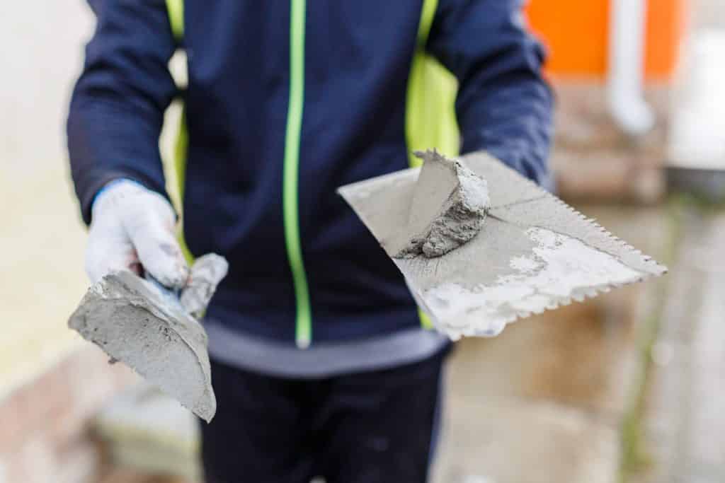 Worker holding trowel with wet cement.