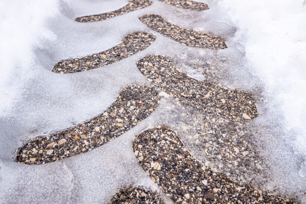 Footprints melting through snow on pavement.