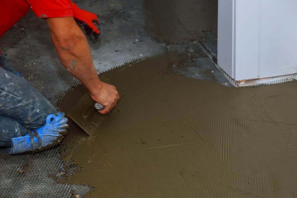 Worker smoothing concrete floor near white object.