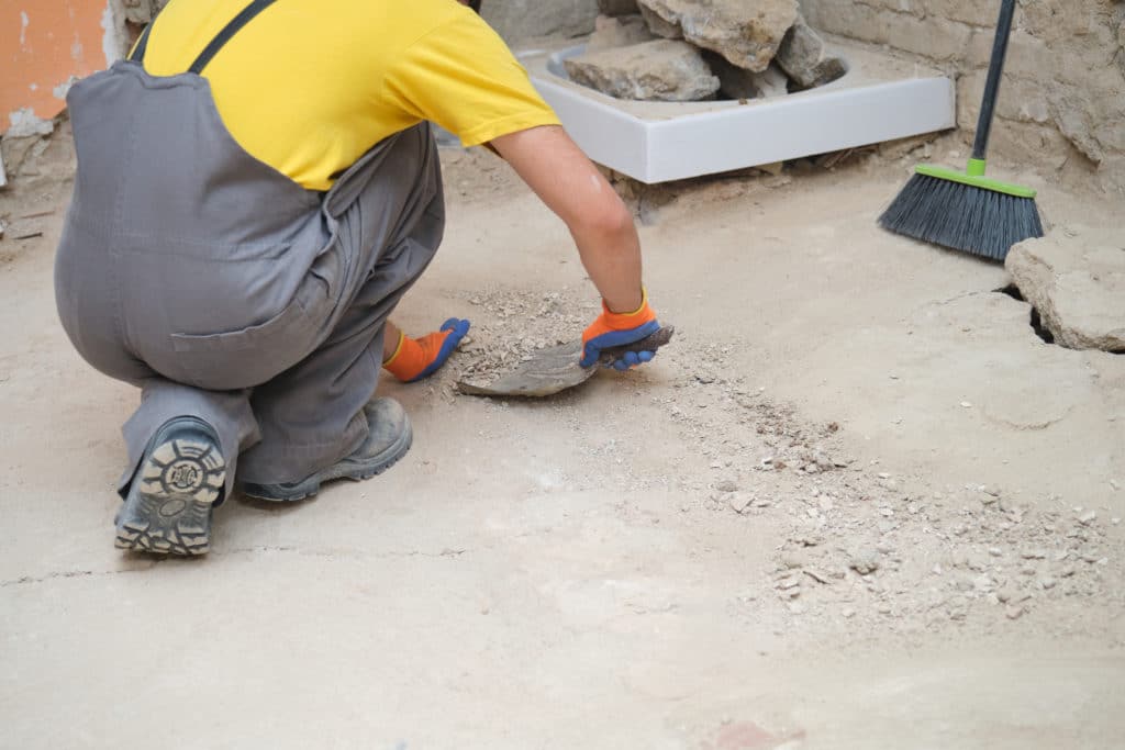 Worker kneeling and cleaning construction debris.