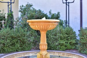Ornate garden water fountain with bushes.