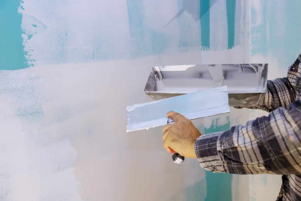 Person applying drywall joint compound with taping knife.