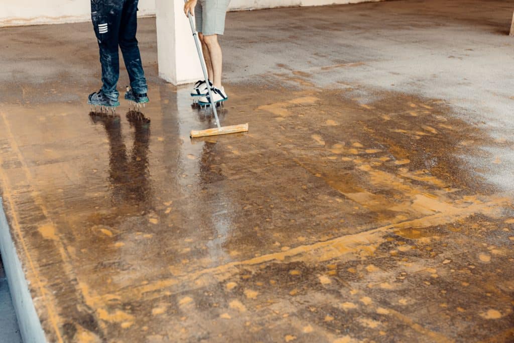 Workers cleaning wet concrete floor with squeegees.