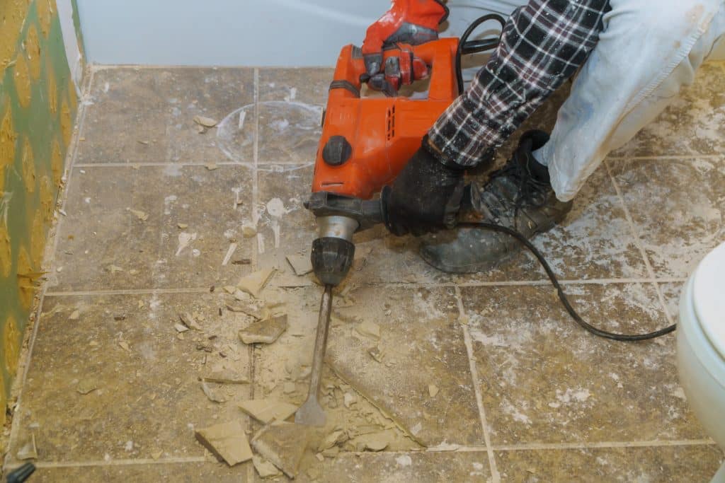 Worker using jackhammer for bathroom tile removal.