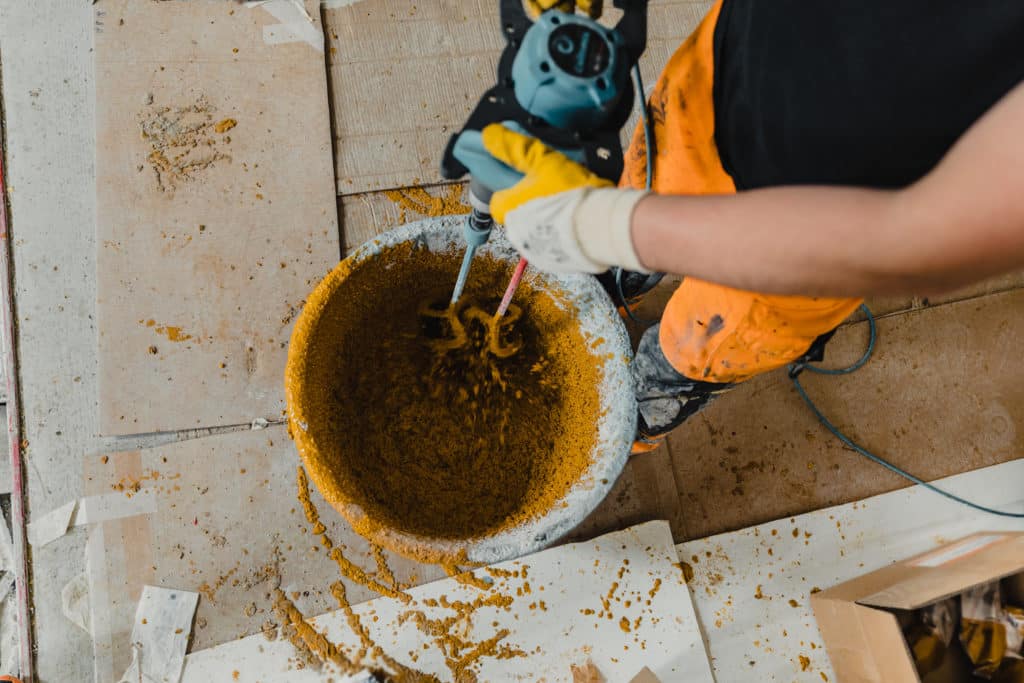 Worker mixing concrete with electric drill.