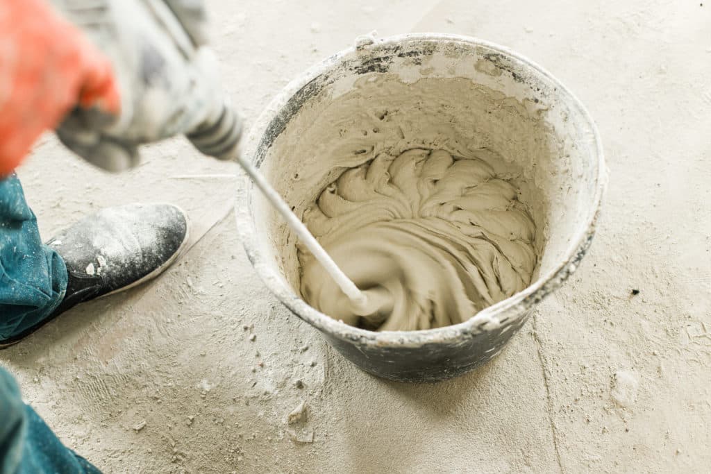 Worker mixing concrete with power drill.