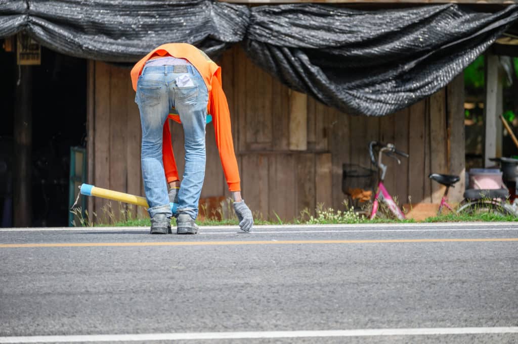 Worker marking road with paint for traffic lines.