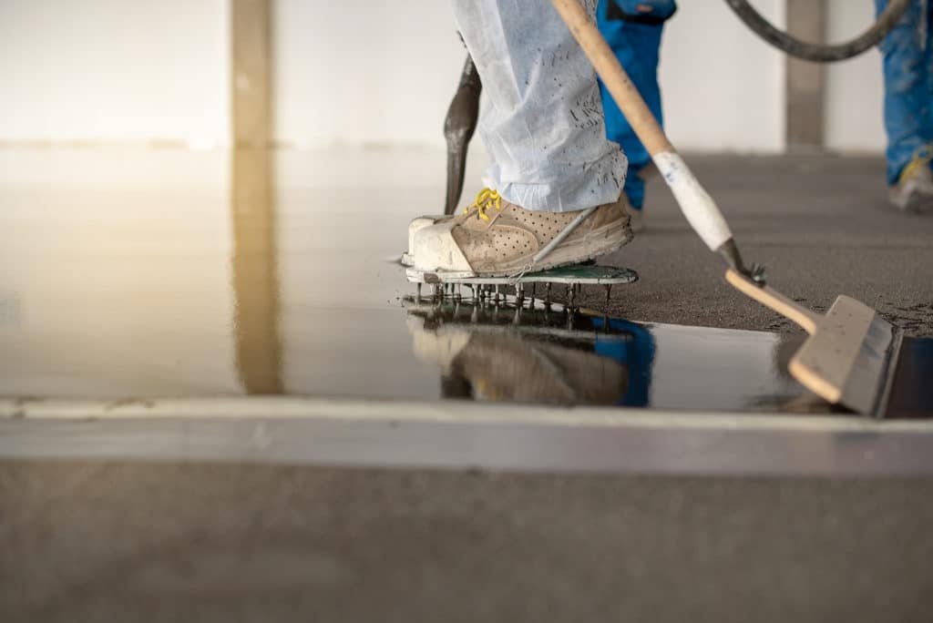 Worker smoothing concrete with trowel and spiked shoes.