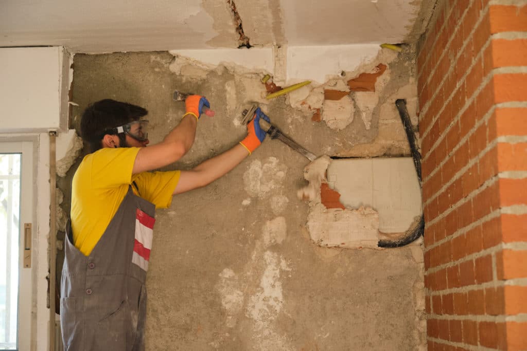 Worker chiseling wall during renovation work.