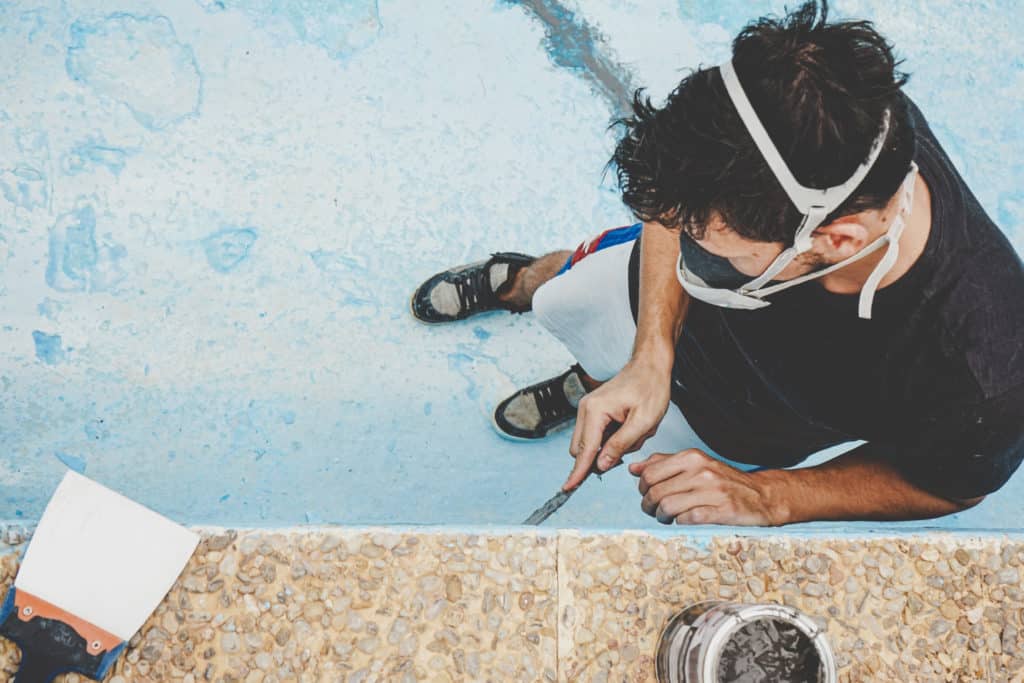 Man repairing pool edge, wearing face mask.