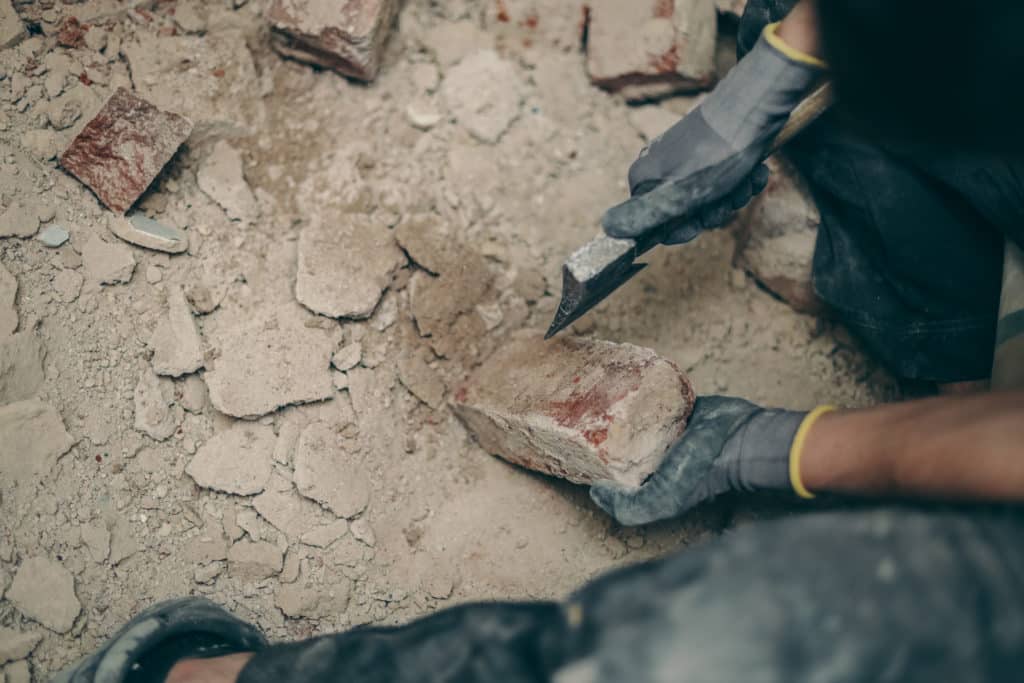 Person chiseling a brick at construction site.